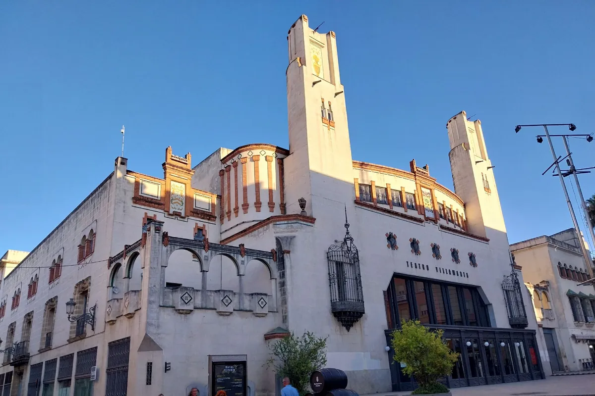 The cream and brick front of the Teatro Villamarta in Jerez, with two tall towers, arched windows and a blue sky